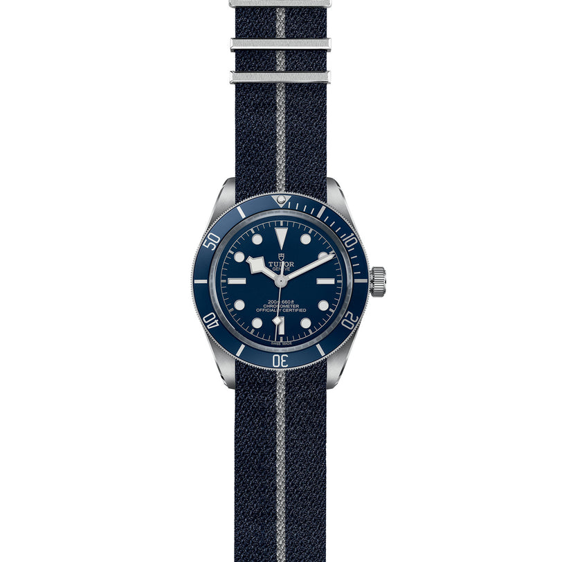 The TUDOR Black Bay 58 is a navy blue diving watch with a round face, white hour markers, rotating bezel, striped fabric strap, and self-winding mechanical movement.