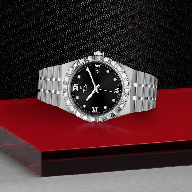 A TUDOR Royal wristwatch with a black dial, silver Roman numerals, and a date display is set against a red and black geometric background, showcasing the sport-chic style of TUDOR’s automatic watches.