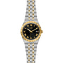 The TUDOR Royal is a two-tone automatic watch featuring a black dial, gold Roman numerals, gold bezel, and an integrated stainless steel and gold bracelet. It displays the date at 3 o’clock.