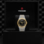 A TUDOR Royal wristwatch with a black and gold dial and integrated bracelet is displayed upright in a black Tudor presentation box, highlighting the Royal’s automatic sport-chic style.