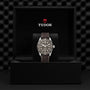 A TUDOR Black Bay 58 925 with a dark strap is displayed upright in an open black box showing the TUDOR logo and name on the inside lid. This stylish divers watch features a 39 mm case.