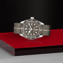 A TUDOR Black Bay 58 925 divers watch with a gray leather strap and gray dial is displayed on a red and black geometric surface against a textured black background.