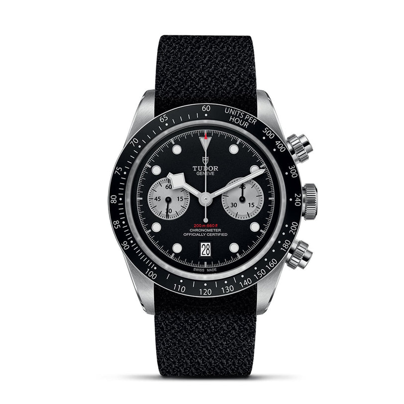 The TUDOR Black Bay Chrono features a black dial, two silver subdials, a black bezel, date display at 6 o’clock, and a sleek black fabric strap.
