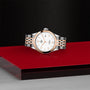 The TUDOR 1926, an elegant two-tone wristwatch with a silver and rose gold bracelet, is displayed on a glossy red-and-black platform set against a textured dark background.