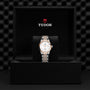 The TUDOR 1926 wristwatch, with a silver and gold bracelet, is elegantly showcased upright in a black box featuring the TUDOR logo on the inside lid.