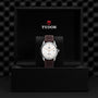 A TUDOR 1926 wristwatch with a brown leather strap is displayed in an open black box featuring the TUDOR logo.
