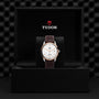 A TUDOR 1926 wristwatch with a white dial and brown leather strap is showcased in an open black TUDOR presentation box.