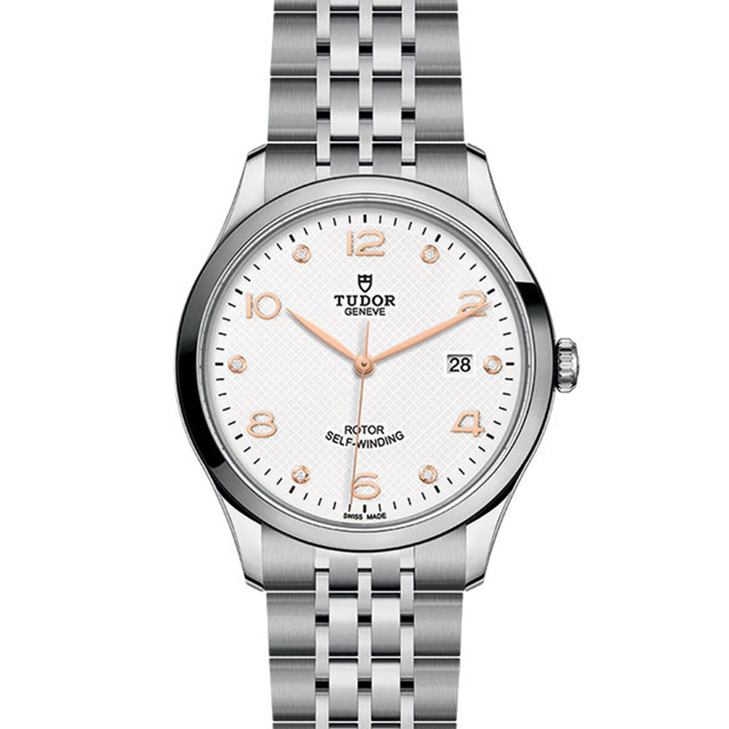 The TUDOR 1926 is a classic silver wristwatch featuring a white textured dial, rose gold hour markers, date window at 3 o’clock, and a metal link bracelet.