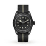 The TUDOR Black Bay Ceramic is a Swiss-made wristwatch featuring a black dial, luminous markers, black bezel, and a black fabric strap with a single beige stripe.