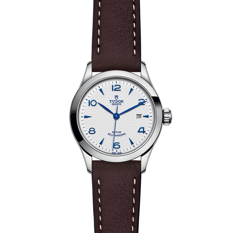 The TUDOR 1926 wristwatch features a white dial with blue numerals, date display at 3 o’clock, silver bezel, and a brown leather strap with white stitching—highlighting classic mechanical watch elegance.