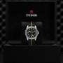A neo-vintage TUDOR Black Bay Pro wristwatch with a black and yellow strap is displayed in an open black box featuring the TUDOR logo inside, reflecting the enduring legacy of TUDOR divers’ watches.