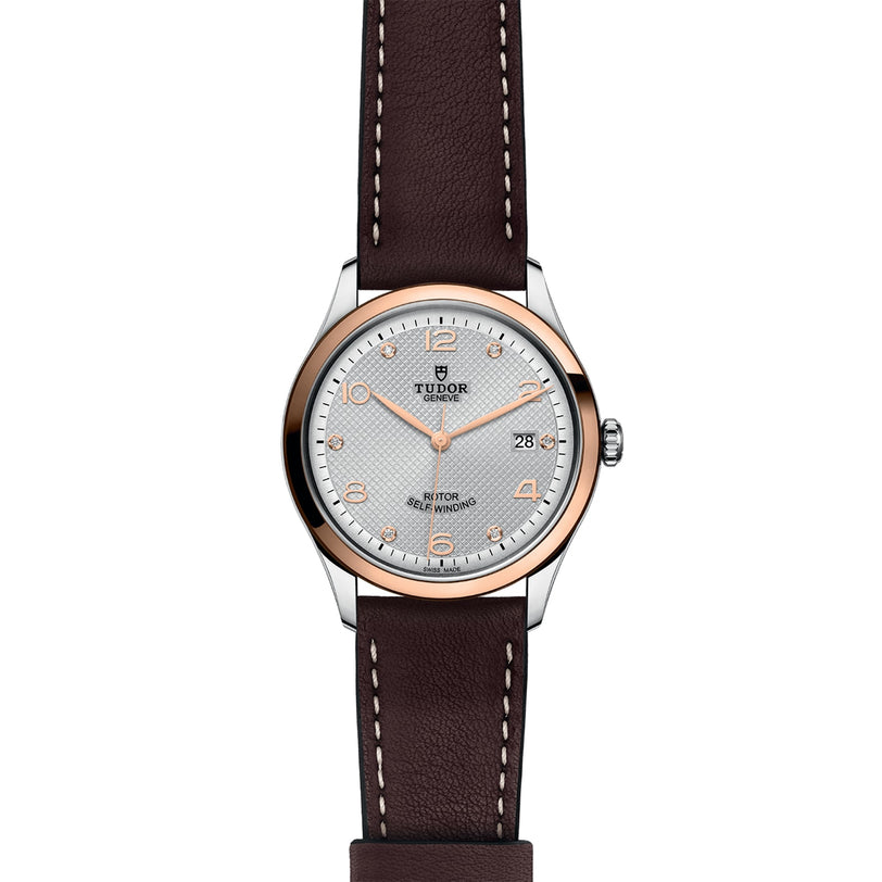 The TUDOR 1926 features a brown leather strap, silver dial, gold bezel, and gold hour markers.