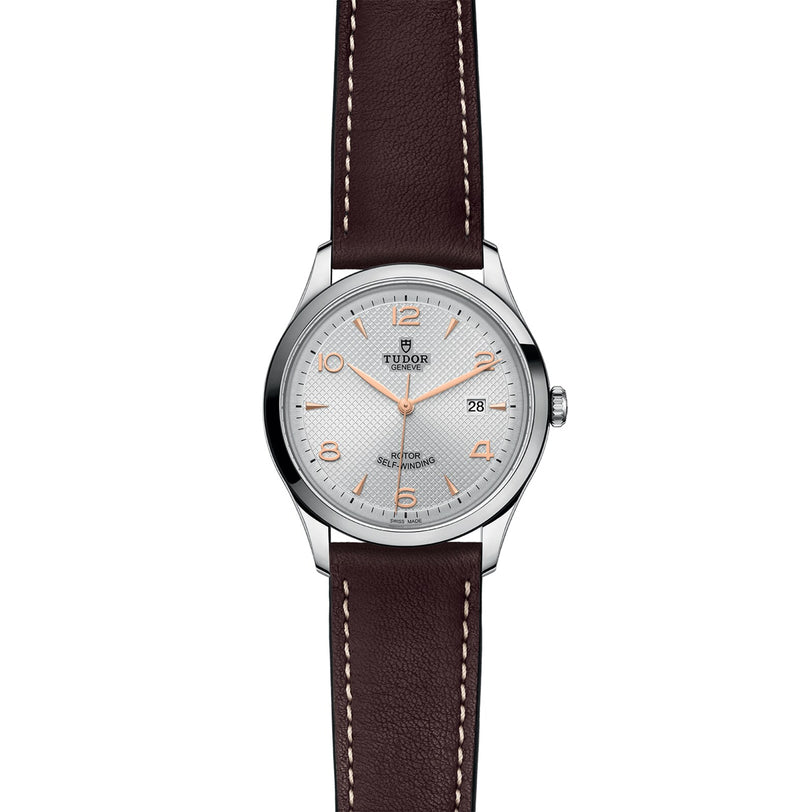 The TUDOR 1926 is a silver wristwatch featuring a white dial, gold hour markers, date at 3 oclock, and a brown leather strap—reflecting traditional mechanical watchmaking from the founder of Rolex.