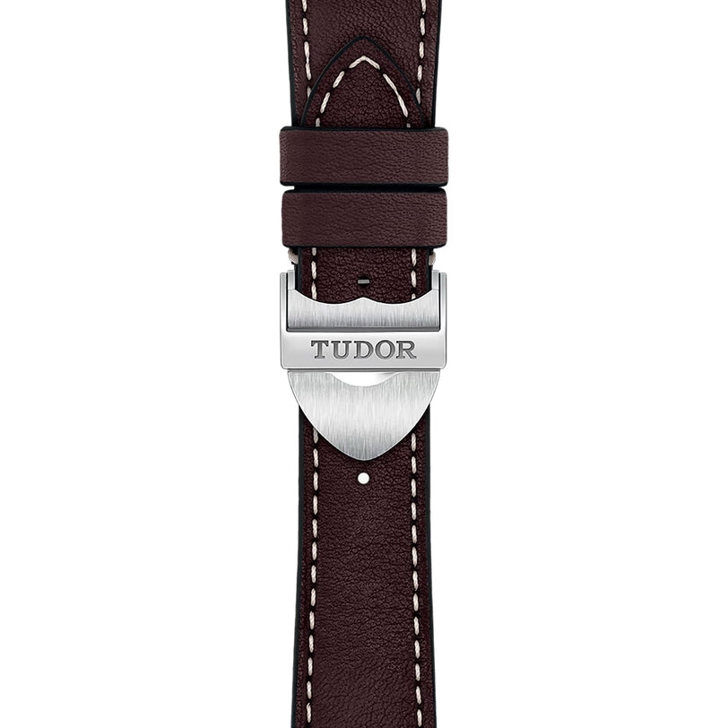 Close-up of a brown leather watch strap with white stitching, featuring a silver clasp engraved with TUDOR—an elegant detail of the TUDOR 1926 collection.