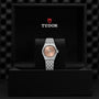 A TUDOR Royal wristwatch is showcased in an open black Tudor-logo box, featuring a salmon dial, automatic movement, and metal bracelet that emphasize its sport chic elegance.