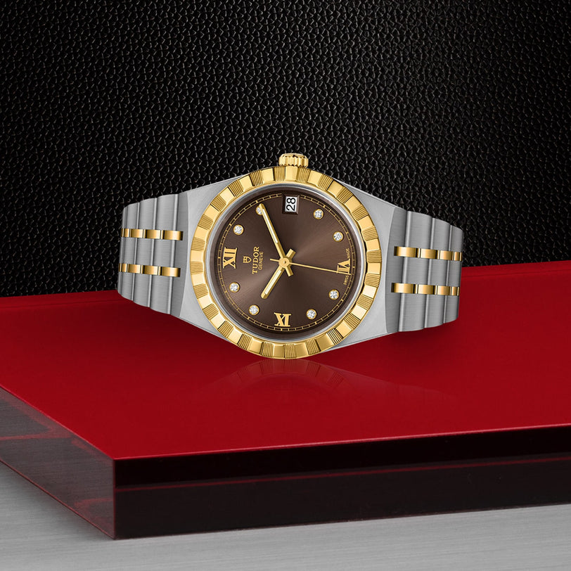The TUDOR Royal wristwatch features a brown dial with gold Roman numerals and diamond hour markers, automatic movement, and a two-tone design, presented on a red and black geometric surface for a sport chic style.