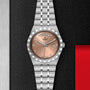 A TUDOR Royal wristwatch with a salmon dial, silver markers, day-date display, and stainless steel bracelet is shown on textured black, highlighting its sport-chic elegance.