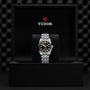 A TUDOR Black Bay 31 with a black dial and silver bracelet is displayed in an open black box bearing the TUDOR logo inside the lid, showcasing unisex chic style and the precision of Manufacture Calibres.