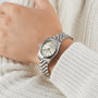 A TUDOR Black Bay One 31 wristwatch with a metal band on a persons wrist, paired with a white knitted sweater.