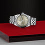 A TUDOR Black Bay One 31 wristwatch with a silver case and champagne dial, displayed on a red and black platform.