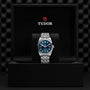 A stylish TUDOR Black Bay One 36 stainless steel wristwatch with a blue dial is showcased on a cushion inside an open black box bearing the TUDOR logo.