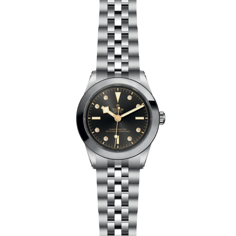 The TUDOR Black Bay One 39 is a stainless steel wristwatch with a black dial, gold-tone markers and hands, a five-link bracelet, the Tudor logo, and precise Manufacture Calibres—offering unisex chic style.