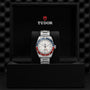 A TUDOR Black Bay GMT wristwatch with a red and blue bezel, opaline dial, and silver band is displayed in an open black TUDOR box, highlighting its iconic GMT function.