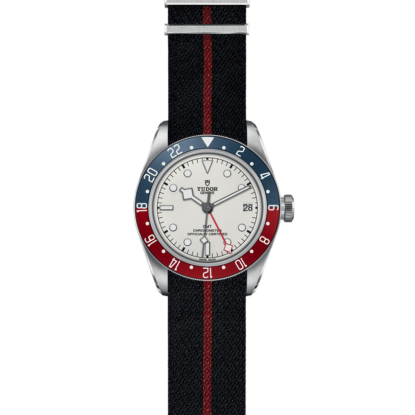 The TUDOR Black Bay GMT features an opaline dial, blue and red bezel, black strap with red stripe, multiple time zone function, and a date display at 3 o’clock.