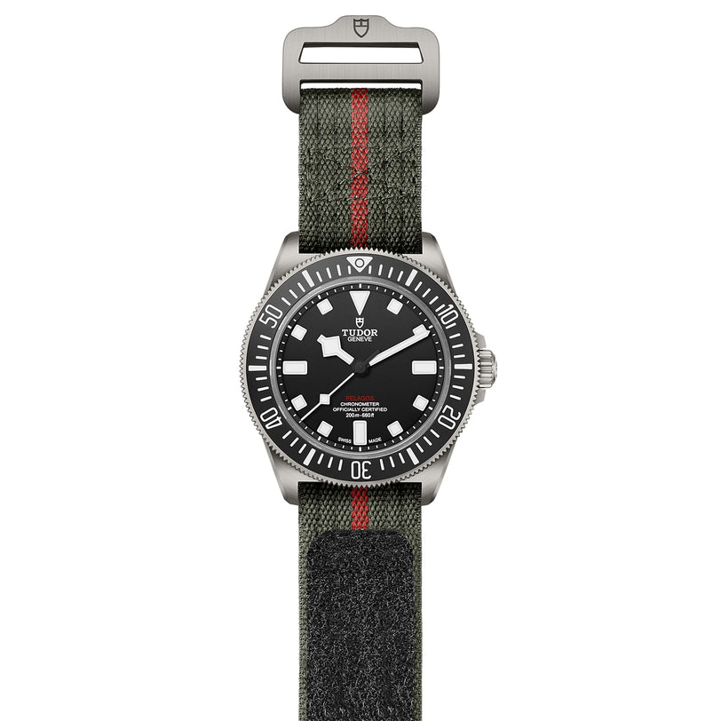 The TUDOR Pelagos FXD watch features a black dial, luminous markers, a rotating bezel, and a green fabric strap with a bold red stripe, inspired by classic TUDOR diving watches.