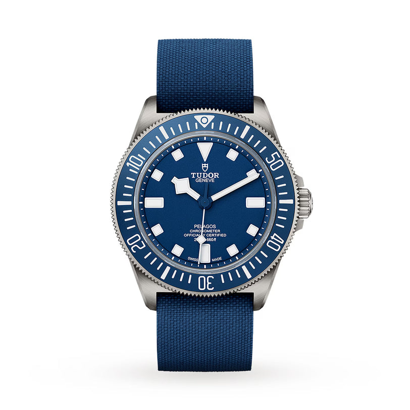 The TUDOR Pelagos FXD dive watch features a blue fabric strap, silver bezel, and white markers, displayed on a white background.