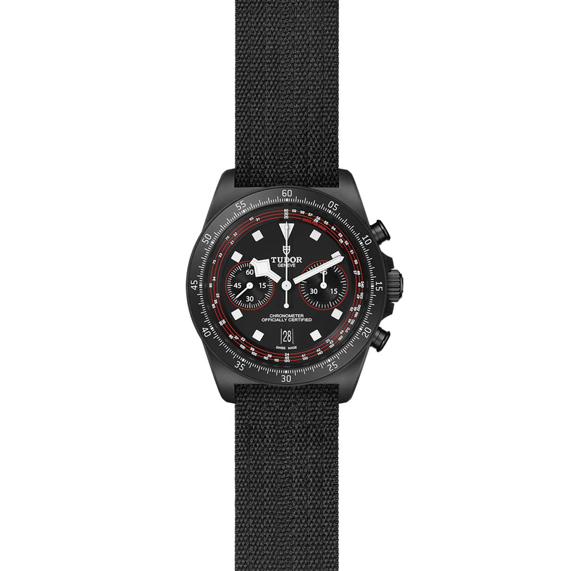The TUDOR Pelagos FXD Chrono is a black cycling-themed chronograph with a textile strap, black dial, white hour markers, red accents, three subdials, date at 6 o’clock, and a cycling-specific tachymeter scale.