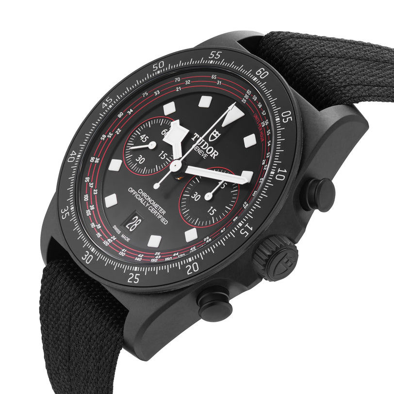 A TUDOR Pelagos FXD Chrono cycling-themed watch with a black case, fabric strap, white indices and hands, and red dial accents, displayed at an angle on a white background.