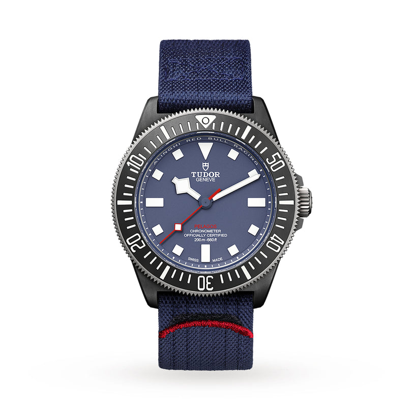 A TUDOR Pelagos FXD wristwatch featuring a blue dial, white hour markers, black bezel, and a blue fabric strap with red stripe, known for underwater navigation functions, shown on a white background.