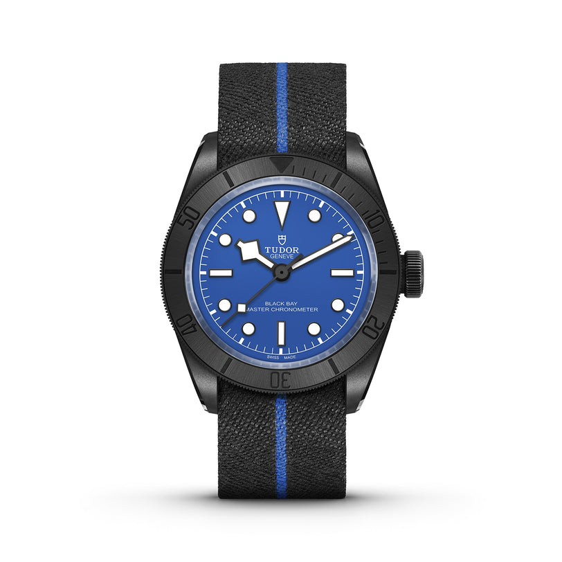 The TUDOR Black Bay Ceramic Blue features a blue dial, black bezel, and signature Snowflake hands on a black fabric strap with a central blue stripe, set against a white background—an iconic TUDOR diver’s watch.