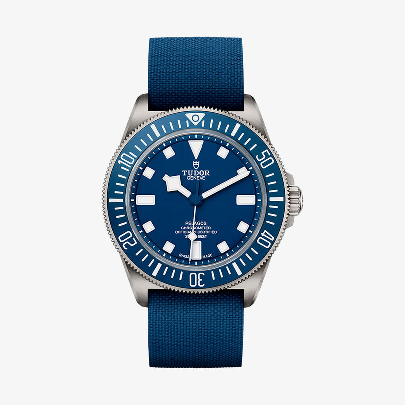 The TUDOR Pelagos FXD is a blue dive watch with a round face, titanium case, rotating bezel, fabric strap, and 200m water resistance, displaying the time 10:11.
