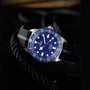 A TUDOR Pelagos FXD watch featuring a titanium case, blue dial, and fabric strap is displayed on black rope with a dark background.