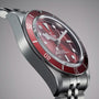 Close-up of a TUDOR Black Bay 58 wristwatch featuring a red bezel and stainless steel bracelet, set against a gray background.