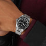 A person wearing a TUDOR Black Bay watch with a stainless steel bracelet and black bezel on their left wrist.