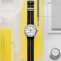 The TUDOR Black Bay Pro wristwatch with a black and yellow strap is displayed on a yellow and white geometric background.
