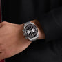 A hand wearing the TUDOR Black Bay Chrono, a silver wristwatch featuring a black dial and three white subdials.