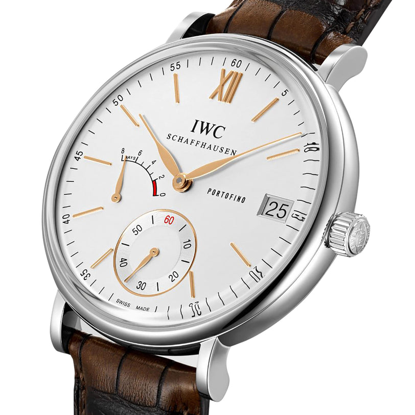 A close-up of the IWC Schaffhausen Portofino Hand-Wound Eight Days watch featuring a white dial, gold markers, date display, power reserve indicator, subdial, brown leather strap, and hand-wound movement.