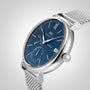 The Portofino Hand-Wound Eight Days by IWC Schaffhausen features a blue dial, mesh band, date display at 3 oclock, and a sub-dial at 6 oclock, displayed against a light grey background.