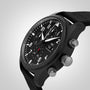 The IWC Schaffhausen Pilots Watch Chronograph Top Gun features a black dial with white numerals, two push buttons, a textured crown, and a black fabric strap, presented on a light gradient background.