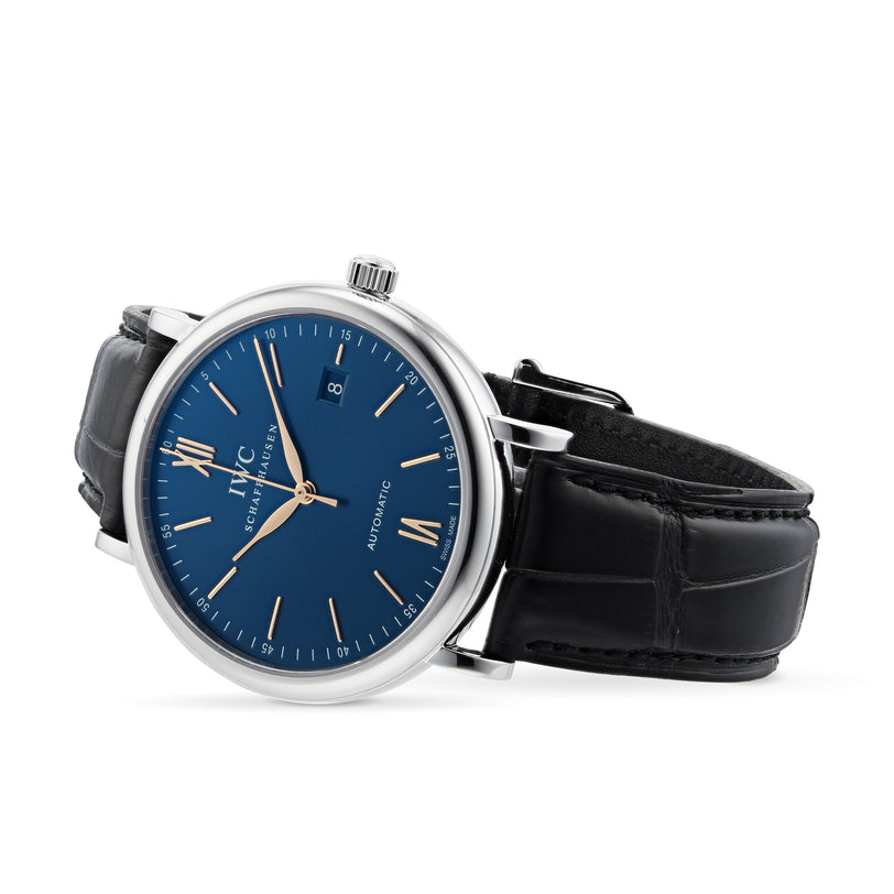 The IWC Schaffhausen Portofino Automatic is a silver analog wristwatch with a blue dial, gold hour markers, black leather strap, and date at 3 o’clock, shown angled against a white background—an example of Swiss precision.