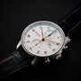The IWC Schaffhausen Portugieser Chronograph, featuring a silver stainless steel case, white dial with gold numbers, two subdials, and a black leather strap, rests on a black surface.