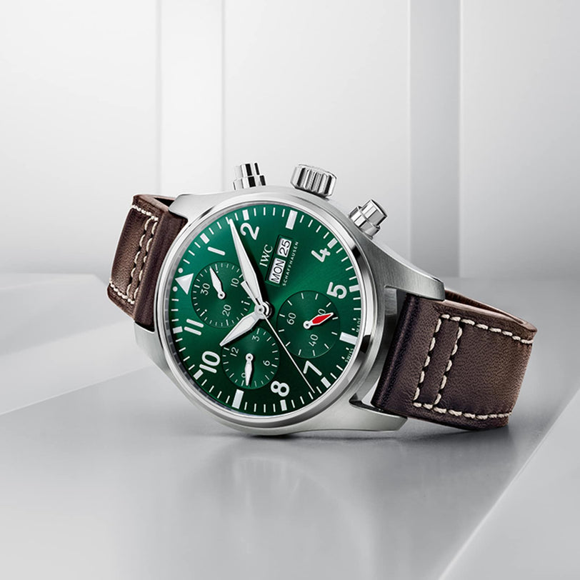 The IWC Schaffhausen Pilots Watch Chronograph 41 features an ergonomic stainless steel case, green dial, brown leather strap, three subdials, and day-date display, elegantly set on a white geometric surface.