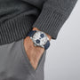 A person in a grey sweater and pants has their hand in their pocket, showing off an IWC Schaffhausen Portugieser Automatic with a white face and blue alligator leather strap.
