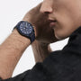 A person wearing an IWC Schaffhausen Pilots Watch Chronograph 41 Top Gun Oceana with a round face and multiple dials holds their hand near their face, partially visible against a plain background.