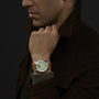 A man wearing a brown jacket displays the Chopard Mille Miglia Classic Chronograph, featuring a green face and tan leather strap.