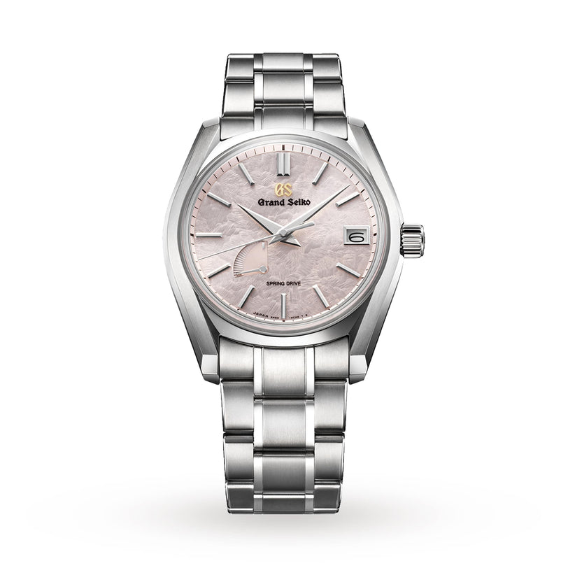 The Grand Seiko Spring Drive Heritage is a silver wristwatch with a textured light pink dial, date display, and metal bracelet.